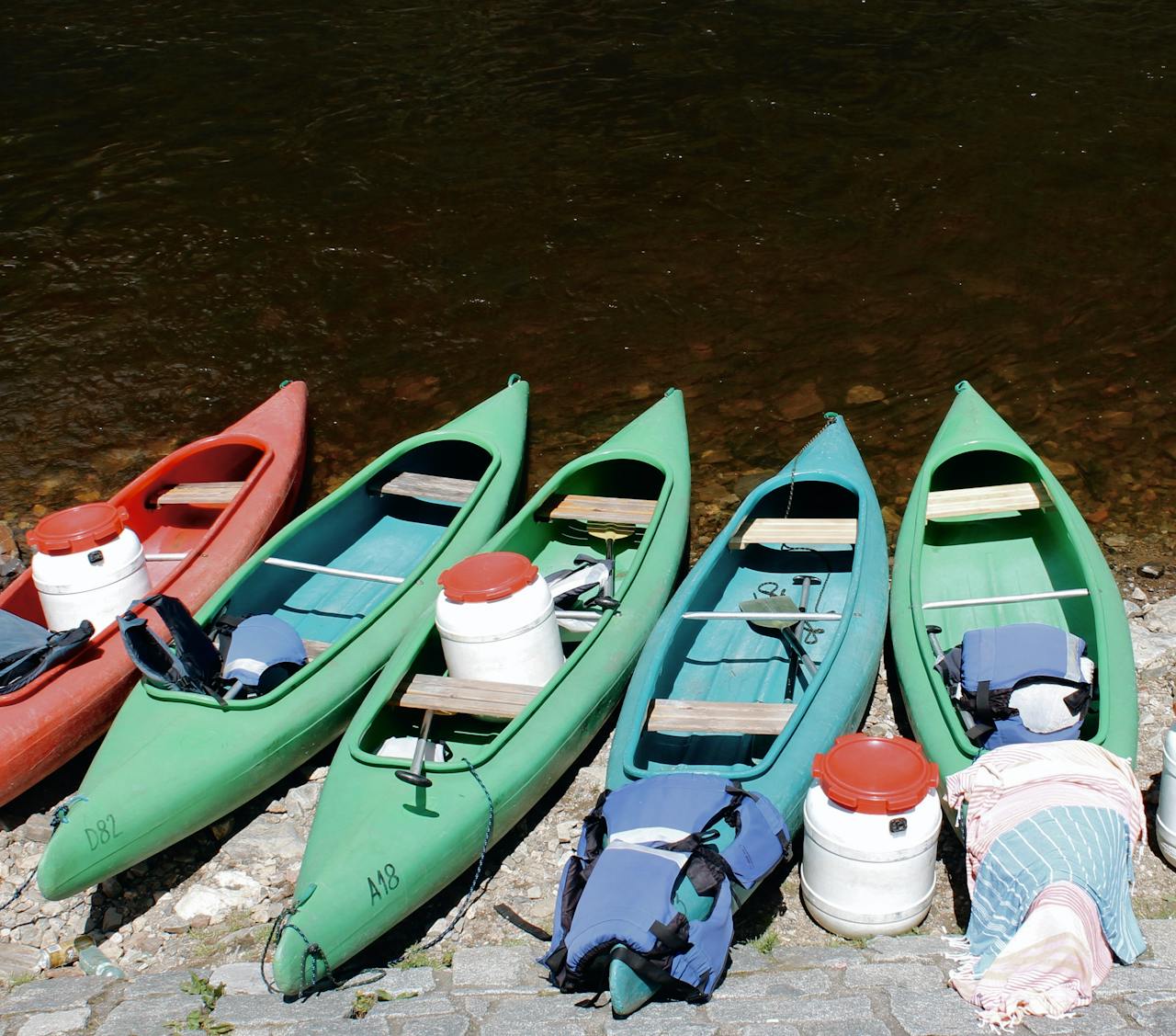 Green and red canoes lined up on a rocky shore in Český Krumlov, ready for adventure.