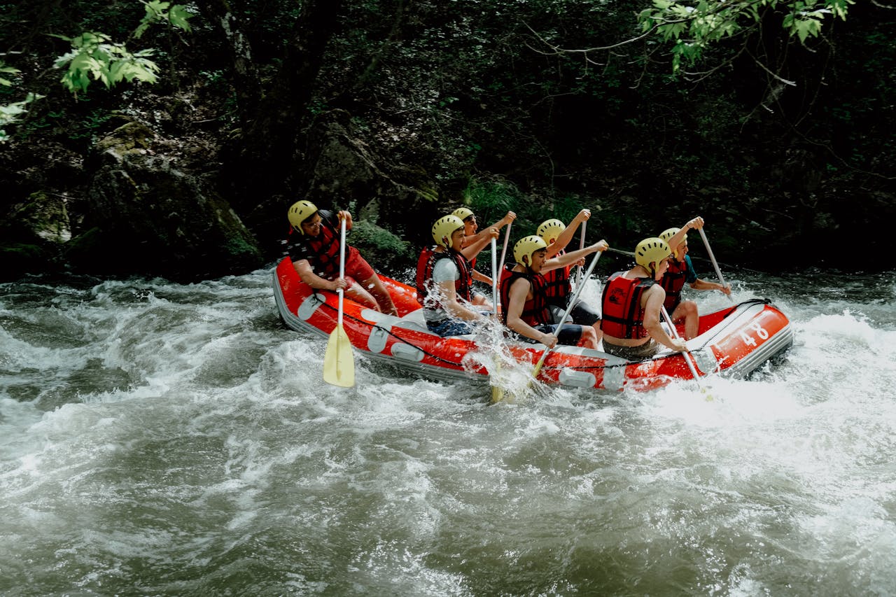 Group of people enjoying a thrilling white water rafting ride through a river surrounded by trees.