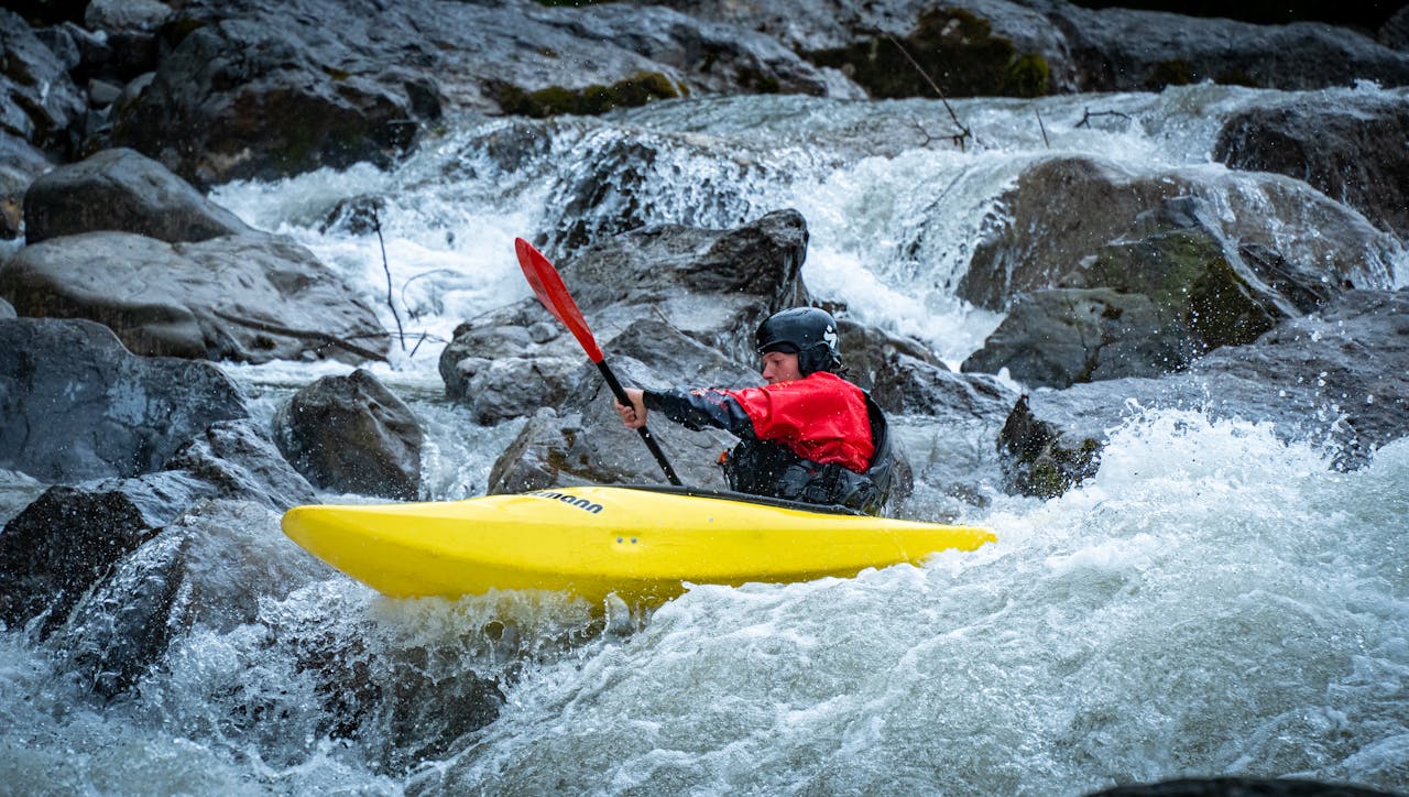 A kayaker skillfully maneuvers through rocky rapids in a vibrant yellow kayak.